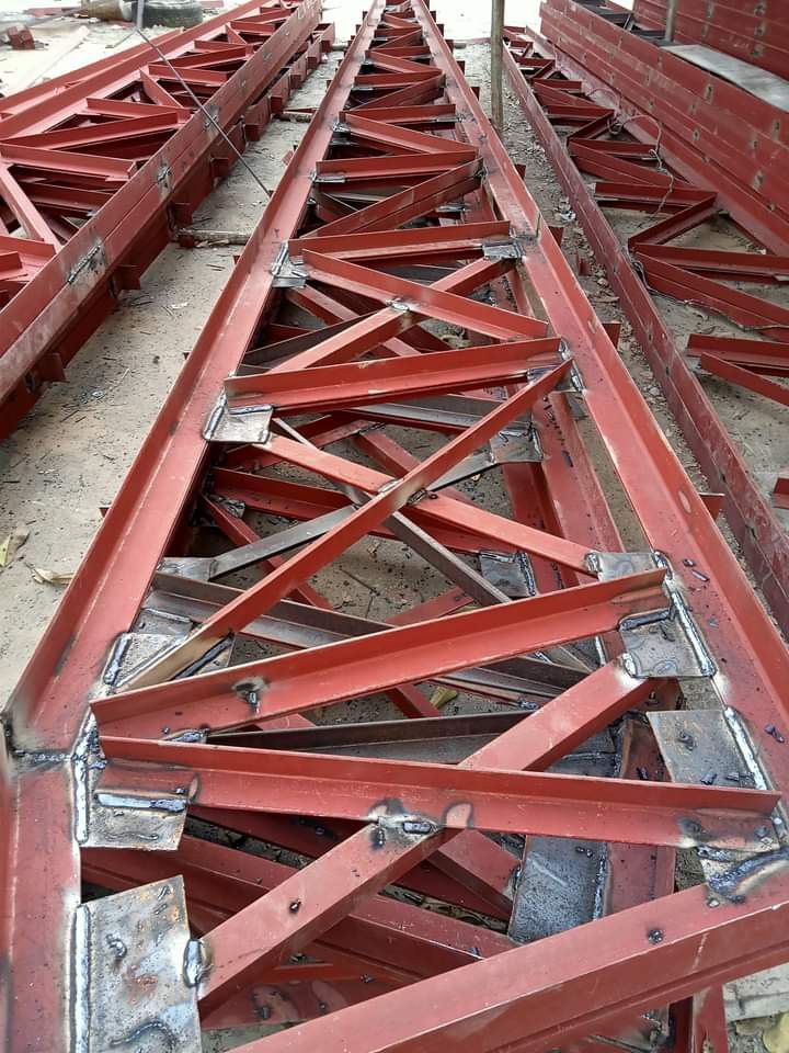 Primer-coated structural steel truss members stacked before erection