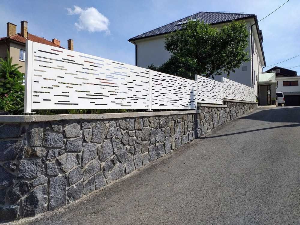 White laser-cut decorative metal fence panels mounted on a stone boundary wall